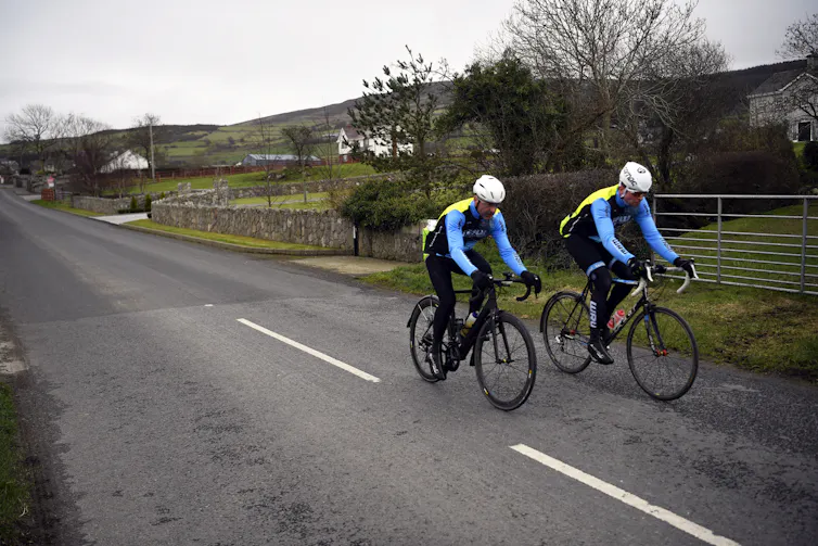 Two cyclists wearing helmets ride down a country road.