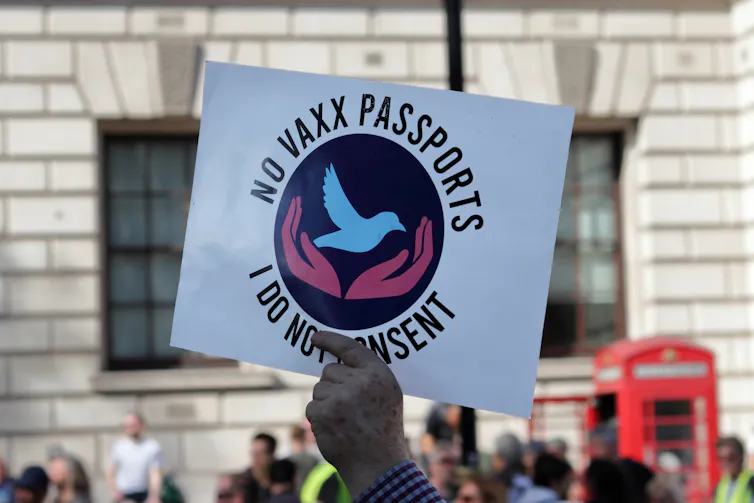 A person holding a sign saying 'No vaxx passports, I do not consent'