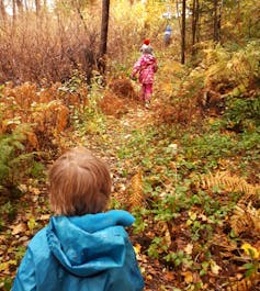 Young children in a colourful autumn leafy forest seen walking up a hill.