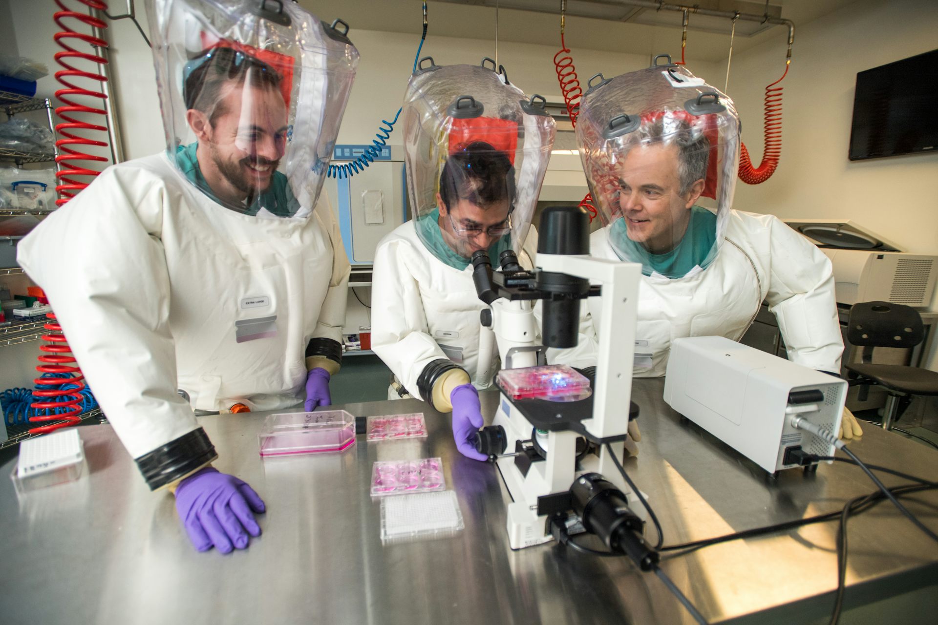 Three scientists in full PPE gather around lab equipment