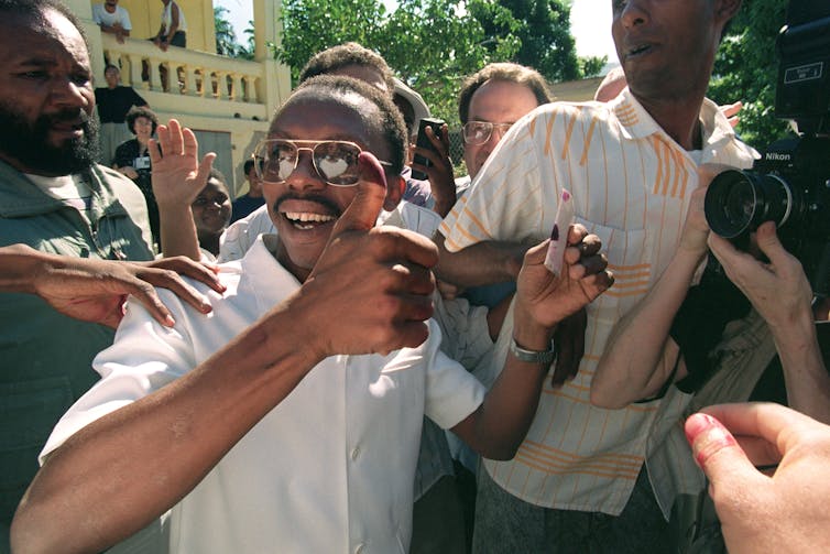 El padre Jean-Bertrand Aristide levanta el pulgar cubierto de tinta después de votar.