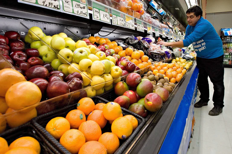 A grocery store worker tends to rows of fruit and vegetables.