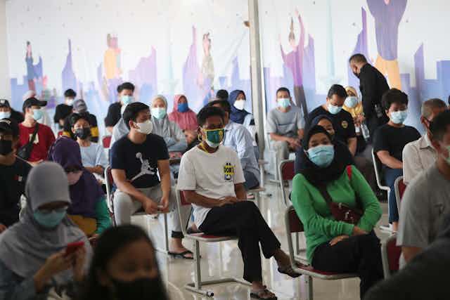 People in Indonesia sit on chairs, waiting for vaccines.