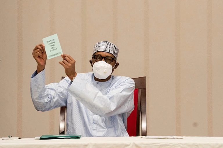Man wearing face mask, seated, holding up a piece of paper