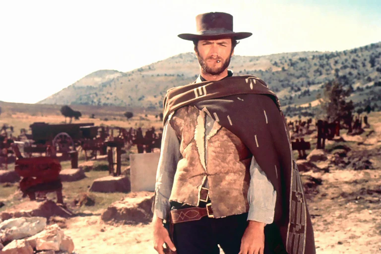 A cowboy stands in a desert and mountainous landscape.