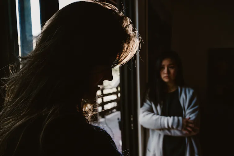 Woman sits with arms crossed in the shadows