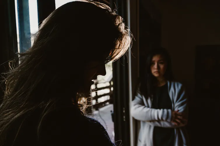 Woman sits with arms crossed in the shadows