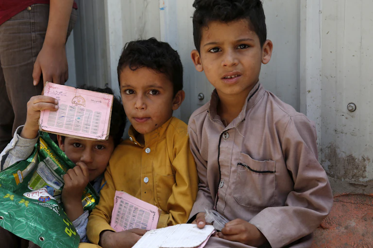Three Yemeni children shown waiting for food rations.