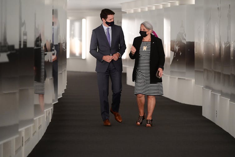 A man and a woman, both wearing masks, walk down a hallway