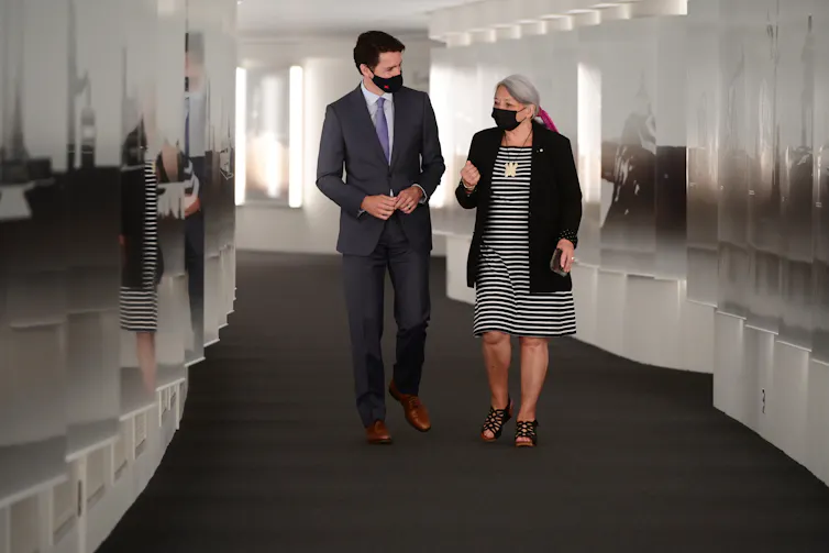A man and a woman, both wearing masks, walk down a hallway