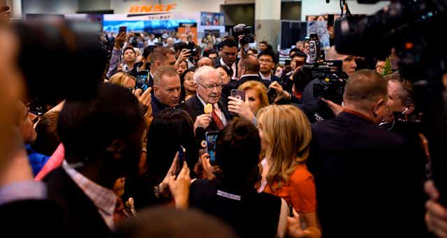 Warren Buffett, thronged by members of the media