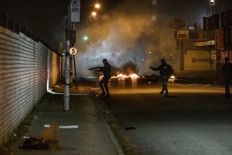 Armed men in a dark street, with fires in the background