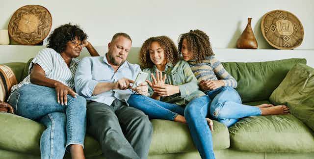 A couple and their two teen daughters sit together on a comfy couch