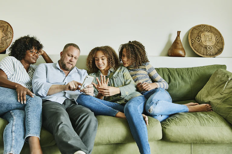 A couple and their two teen daughters sit together on a comfy couch
