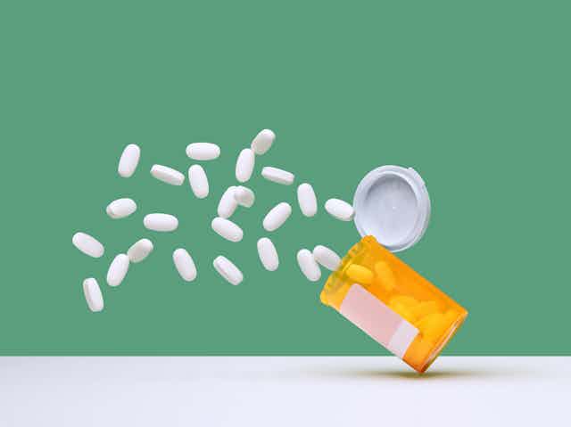 White pills spilling out of falling prescription bottle