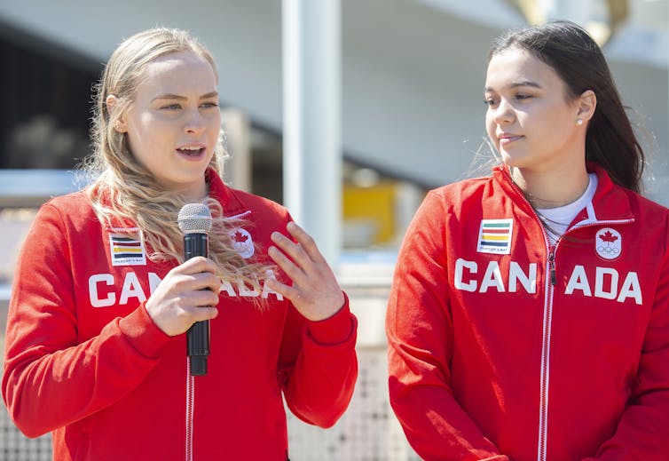 Waist-up shot of two women wearing red zip-up jackets with CANADA spelled across the front.