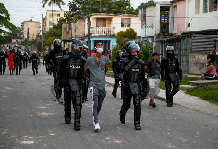 La policía en equipo antidisturbios camina hombre esposado por la calle