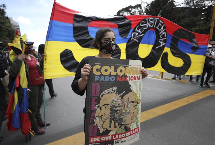 A woman protester holds a sign in front of the Colombian flag