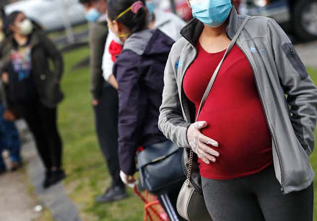 A pregnant woman in a face mask stands in a lineup