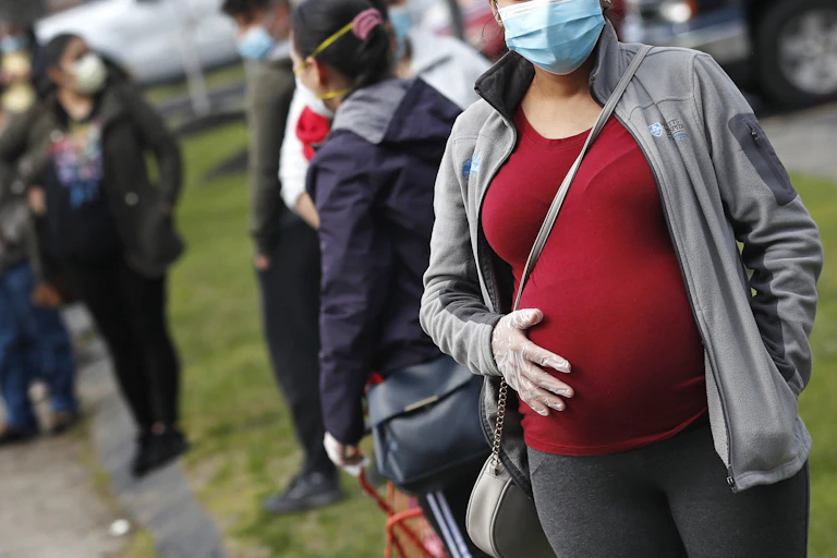 A pregnant woman in a face mask stands in a lineup