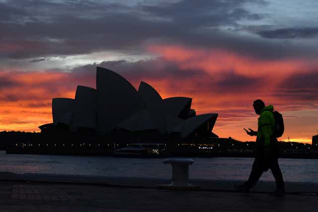 Man walks past Sydney Opera House at dusk.