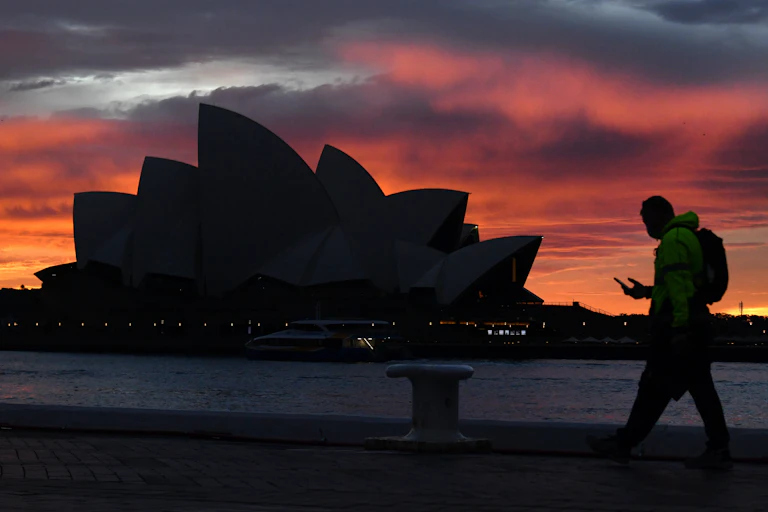 Man walks past Sydney Opera House at dusk.