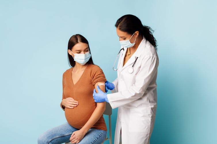 A health-care worker puts a bandage on a pregnant woman's arm after a vaccination