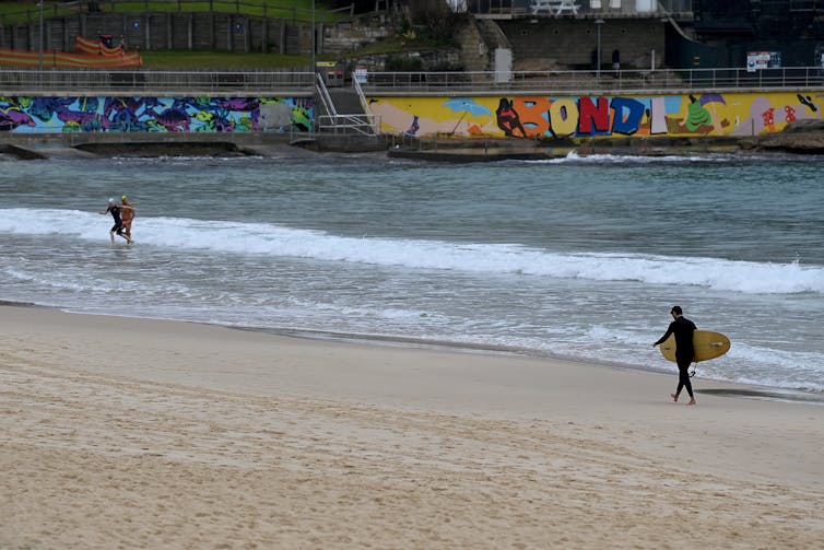 Surfer walks along Bondi beach.