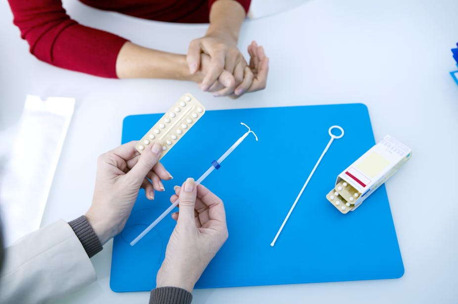 A doctor explaining a woman's birth control options, showing her the pill, and an IUD.