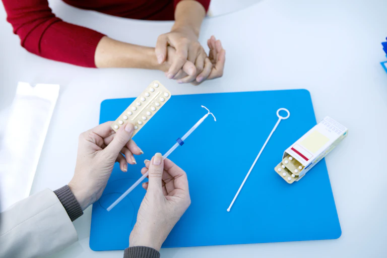A doctor explaining a woman's birth control options, showing her the pill, and an IUD.
