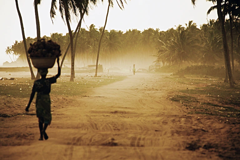 A woman on beach road carrying heavy load.
