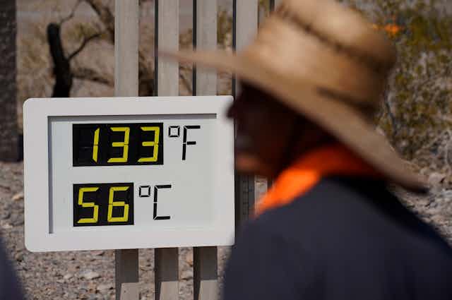 Un homme passe devant un panneau indiquant 56 degrés celcius.