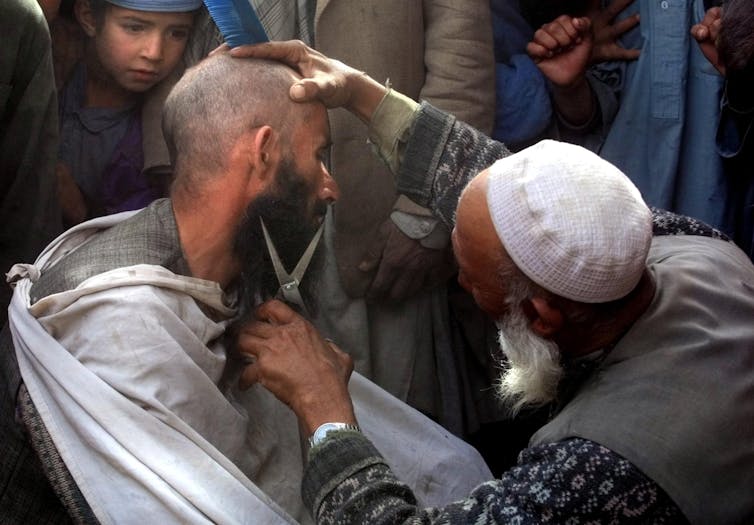 A street hairdresser in Kabul cuts a man's beard.