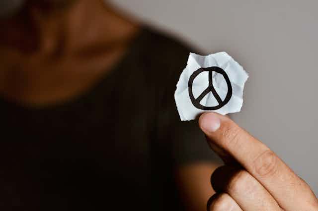 Una mano sujeta un papel con un símbolo de la no violencia dibujado.