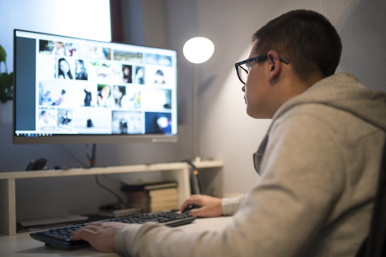 A man looks at a computer screen filled with dozens of faces.