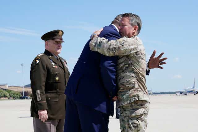 The former top military commander in Afghanistan is hugged upon his return to the US by the defense secretary.
