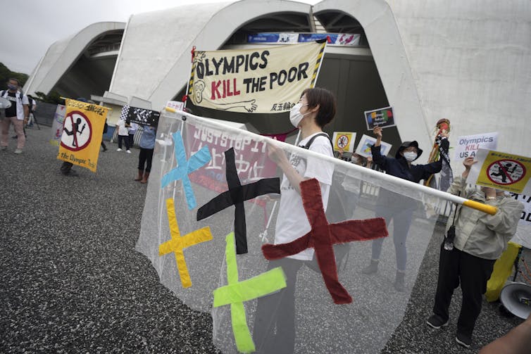 Manifestante segurando uma placa que diz 'Olimpíadas matam os pobres'.