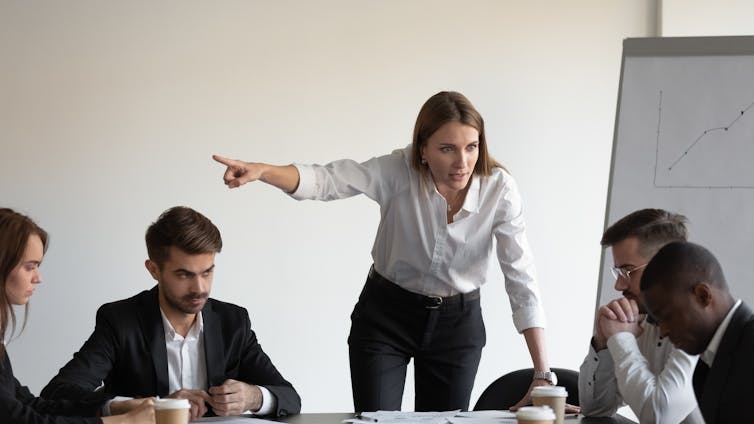 A woman boss yells at her employees in a meeting room.