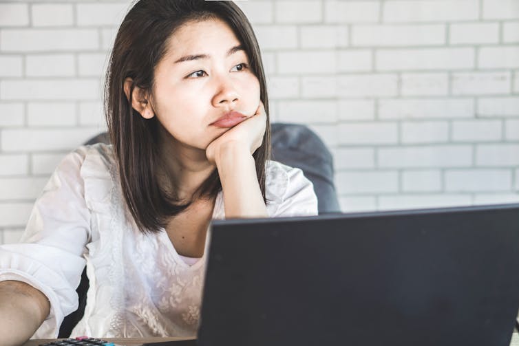 A woman stares forlornly at her laptop.