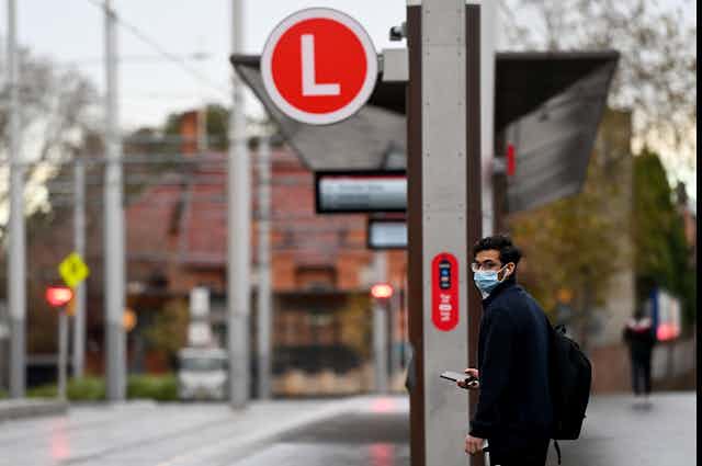 A man waiting at a light rail stop in Sydney wearing a mask.