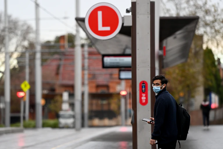 A man waiting at a light rail stop in Sydney wearing a mask.