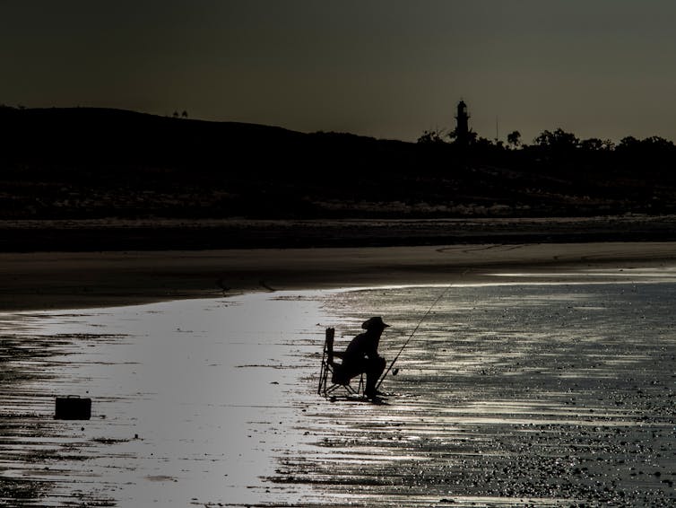 man sits while fishing on beach