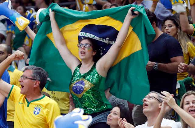 A woman in a Brazilian flag printed top waves a Brazil flag at the Rio Olympics, surrounded by other fans