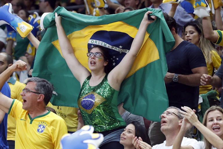 A woman in a Brazilian flag printed top waves a Brazil flag at the Rio Olympics, surrounded by other fans