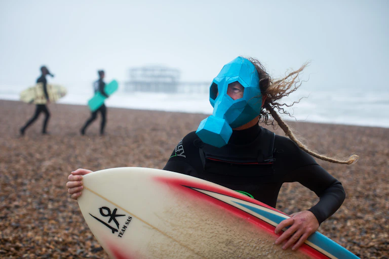 A surfer wearing a gas mask on a shingle beach.