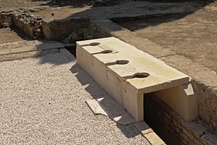 A stone sill overhanging a straight ditch with holes at regular intervals.