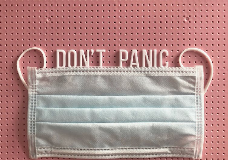A pink noticeboard with a Don't Panic message, along with a facemask