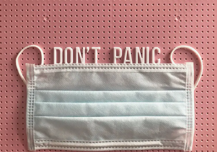 A pink noticeboard with a Don't Panic message, along with a facemask