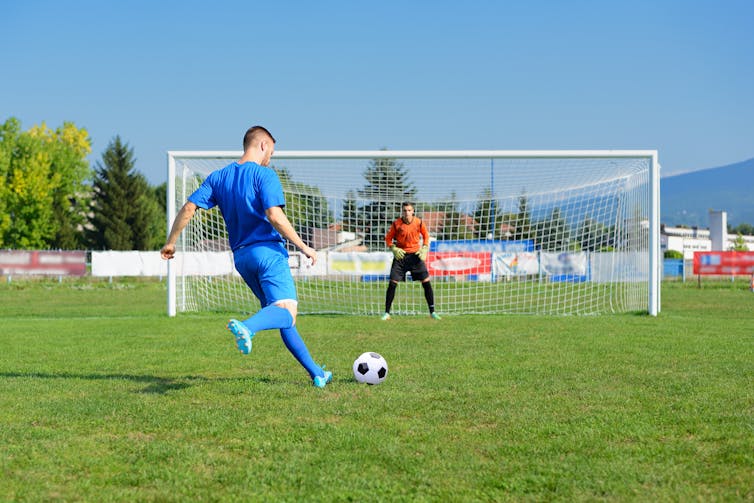 A football player takes a penalty kick, while the goal waits in the net to stop it.