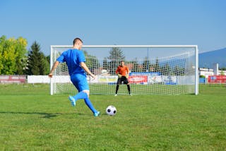 サッカー選手はペナルティーキックを受け、ゴールはネットでそれを止めるのを待つ。